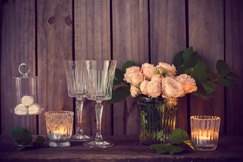 Elegant vintage wedding table decoration with roses and candles near the wall of old wooden board