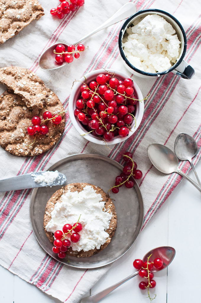 Natural healthy food, grain bread, cottage cheese and fresh organic red currants on a white wooden kitchen table with linen cloth and vintage cutlery. Seasonal berries, rustic breakfast.