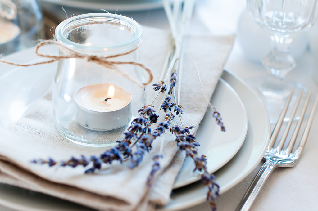 Dining table setting at Provence style, with candles, lavender, vintage crockery and cutlery, closeup.